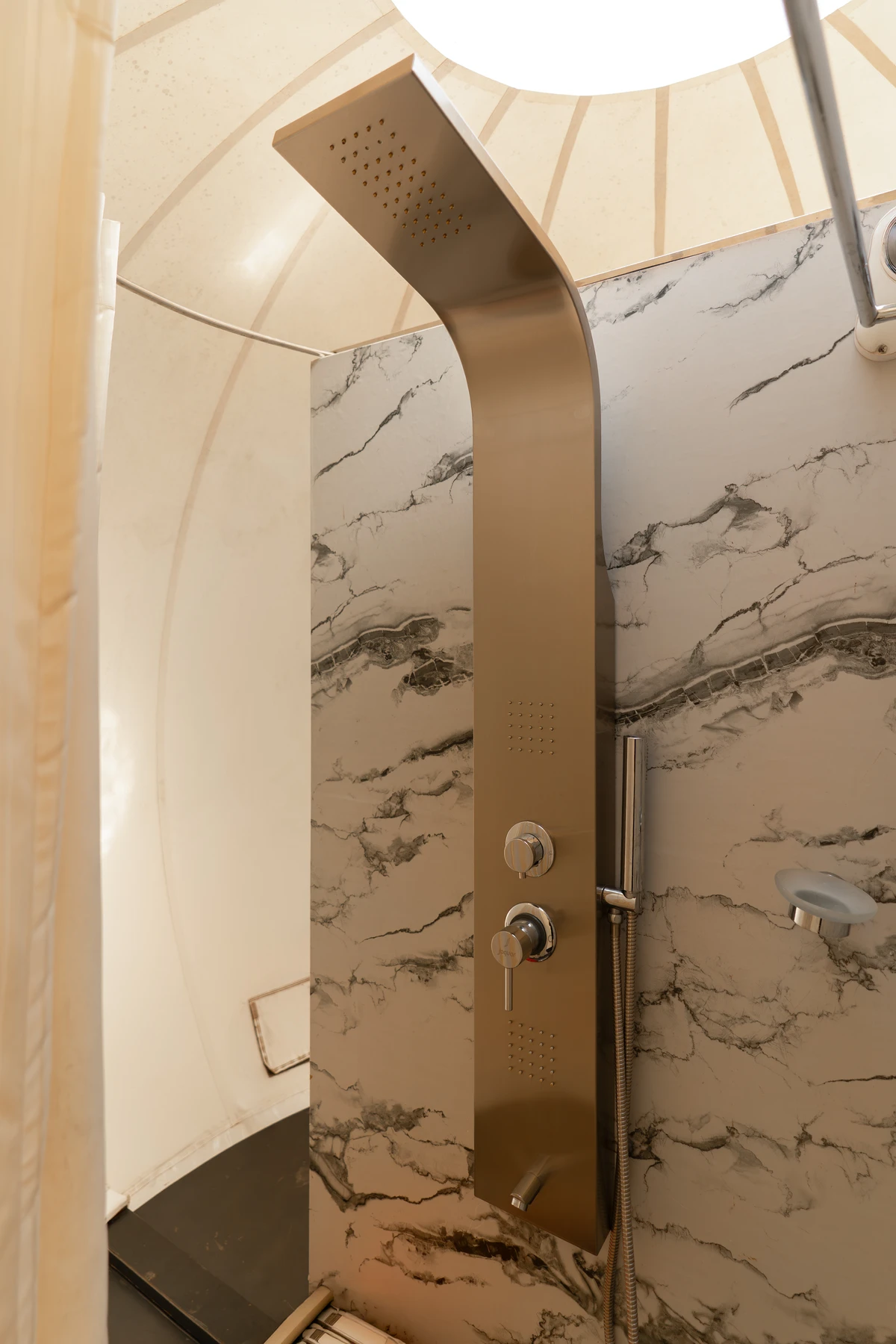 Brushed Metal Shower in Glamping Dome A modern brushed metal shower panel mounted on a white marble-veined wall inside a glamping dome. boche 1000 acre wayanad