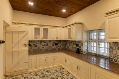 Fully equipped kitchen with classic white cabinets and patterned tiles at boCHE 1000 Acre, one of the best resorts in Wayanad.